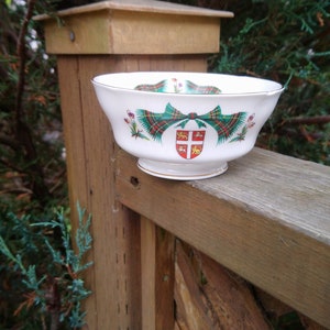 Peut inclure: Un bol en céramique blanche avec un motif tartan vert, rouge et or. Le bol présente un blason avec un lion et une couronne.