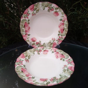 Puede incluir: Dos tazones de sopa de cerámica blanca con un diseño floral con rosas rosas y hojas verdes. Los tazones están apilados uno encima del otro.