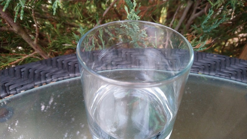 K&ouml;nnte beinhalten: Ein klarer Glasbecher steht auf einer schwarzen und grauen gewebten Oberfl&auml;che. Das Glas ist leer und scheint aus dickem Glas zu sein.