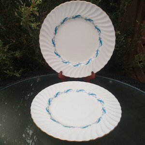 May include: Two white ceramic dinner plates with a blue and white floral design. The plates have a scalloped edge and a gold rim.