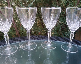 May include: Four clear glass wine glasses with a cut crystal design. The glasses are arranged in a row on a black wicker table.