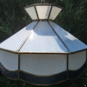 Può includere: Un lampadario da soffitto in vetro bianco e blu con finiture dorate. Il lampadario ha una parte superiore arrotondata a forma di cupola e una parte inferiore a forma di conchiglia.