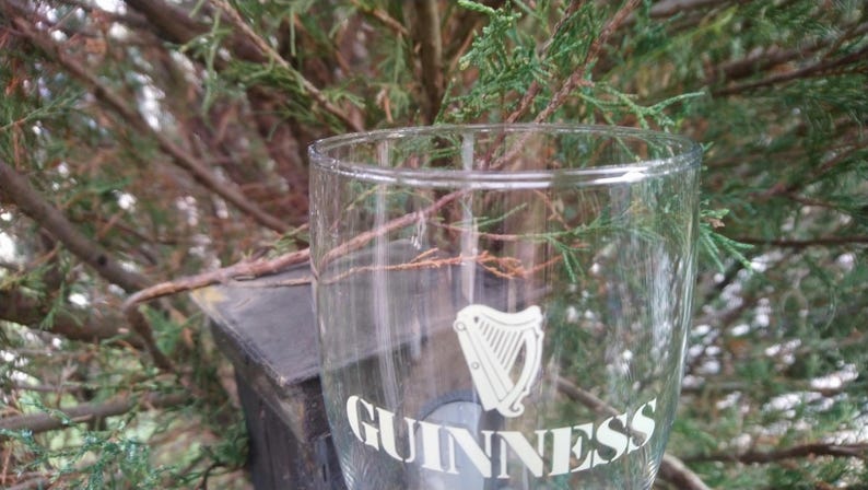 Puede incluir: Un vaso de pinta de vidrio transparente con el logotipo de Guinness y un dise&ntilde;o de arpa impreso en la parte delantera.