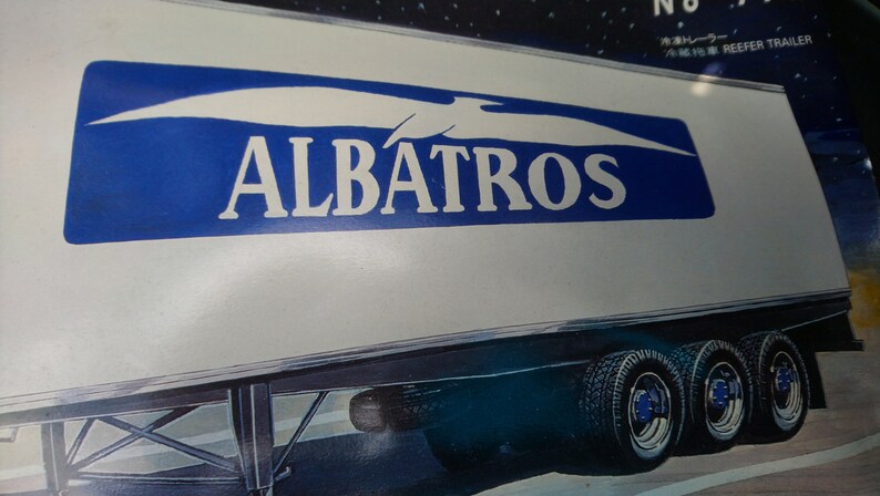 May include: A white refrigerated trailer with the word "ALBATROS" in large blue letters. The trailer has multiple wheels and tires. The image also includes Japanese text.