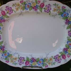 May include: White oval serving platter with a floral border. The border features pink, purple, blue, yellow, and green flowers.