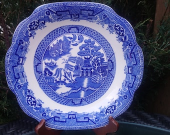 May include: A white ceramic plate with a blue and white willow pattern. The plate has a scalloped edge and is decorated with a traditional Chinese design.