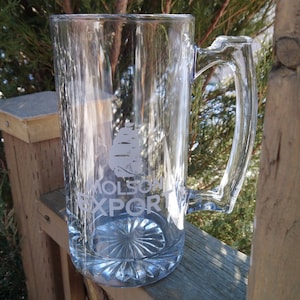 May include: A clear glass beer stein with a frosted design of a ship and the text "Molson Export".