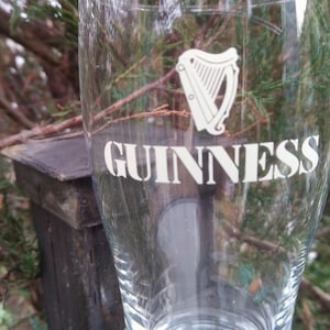 Puede incluir: Un vaso de pinta de vidrio transparente con el logotipo y el texto de Guinness impresos en el lateral. El logotipo presenta un arpa y el texto dice "GUINNESS".