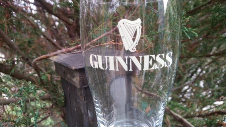 Puede incluir: Un vaso de pinta de vidrio transparente con el logotipo y el texto de Guinness impresos en el lateral. El logotipo presenta un arpa y el texto dice "GUINNESS".