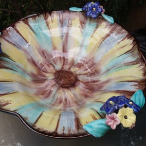 Puede incluir: Un tazón grande de cerámica con un diseño floral amarillo, azul y marrón. El tazón tiene un borde festoneado y está decorado con cuatro acentos de flores azules y amarillas.
