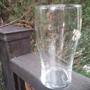 Puede incluir: Un vaso de pinta de vidrio transparente con un borde ligeramente acampanado. El vaso est&aacute; vac&iacute;o y parece estar sobre una superficie de madera.