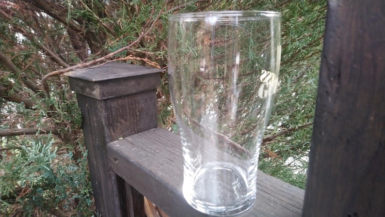 Puede incluir: Un vaso de pinta de vidrio transparente con un borde ligeramente acampanado. El vaso est&aacute; vac&iacute;o y parece estar sobre una superficie de madera.