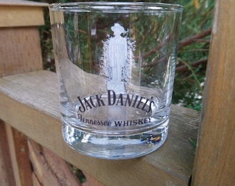 May include: A clear glass tumbler with the Jack Daniel's logo and the words "Tennessee WHISKEY" printed on the bottom. The glass has a white silhouette of a man in a hat etched on the side.