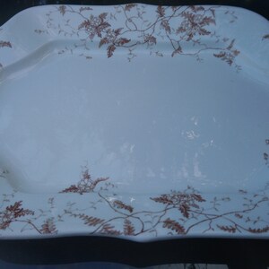 May include: A white oval serving platter with a brown floral design. The platter has a scalloped edge and is ideal for serving a variety of foods.