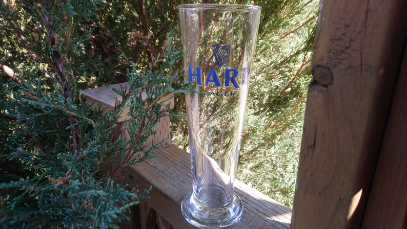 Może przedstawiać: Szklany kufel do piwa z przezroczystego szkła z niebiesko-złotym logo HARP Lager.