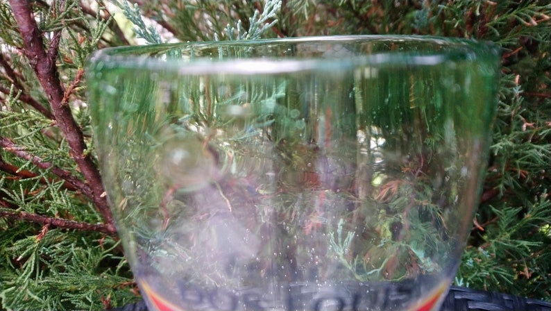 May include: A clear glass with a green rim. The glass is partially filled with a green liquid. The glass is sitting on a table.