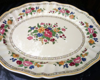 May include: A large, oval serving platter with a cream-colored background and a floral design in shades of red, pink, yellow, blue, and green. The platter has a scalloped edge and a gold trim.