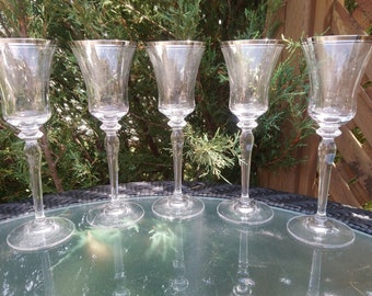 May include: Set of five clear glass wine glasses with a gold rim. The glasses are on a black and white table.