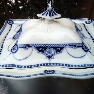 May include: A white porcelain covered dish with a blue and white floral design. The dish has a square base and a domed lid with a finial.
