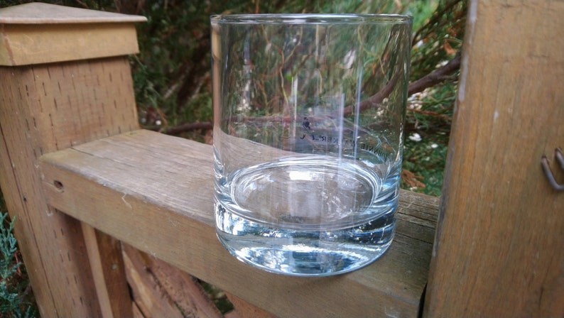 K&ouml;nnte beinhalten: Ein klares Glas mit abgerundetem Boden und geraden Seiten. Das Glas ist leer und steht auf einer Holzoberfl&auml;che.