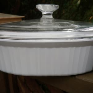 May include: White oval baking dish with a glass lid. The dish has a fluted design and is made of ceramic.