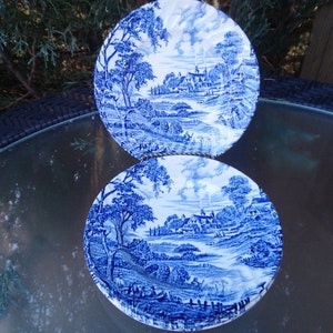 Può includere: Due piatti in porcellana blu e bianca con un design scenico di un villaggio e alberi. I piatti sono impilati uno sopra l'altro.