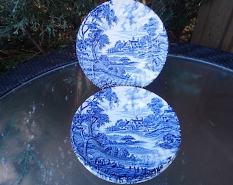 Puede incluir: Dos platos de porcelana azul y blanco con un diseño escénico de un pueblo y árboles. Los platos están apilados uno encima del otro.
