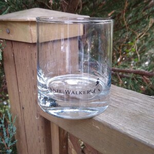 K&ouml;nnte beinhalten: Ein klares Glas mit der Aufschrift "Johnnie Walker" auf dem Boden. Das Glas steht auf einer Holzoberfl&auml;che.