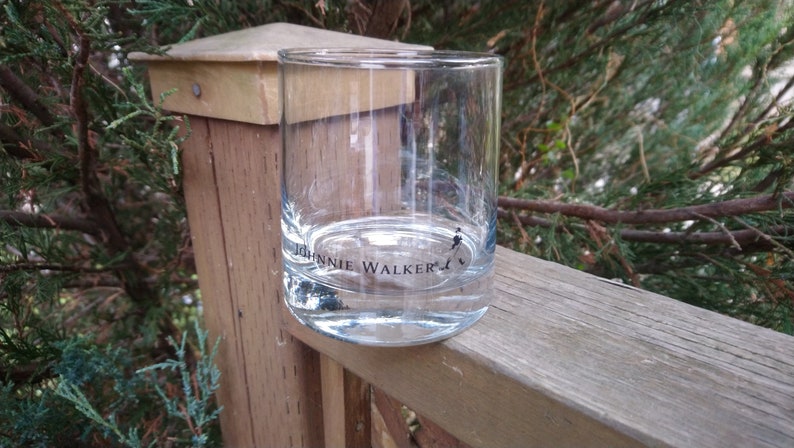 K&ouml;nnte beinhalten: Ein klares Glas mit der Aufschrift "Johnnie Walker" auf dem Boden. Das Glas steht auf einer Holzoberfl&auml;che.