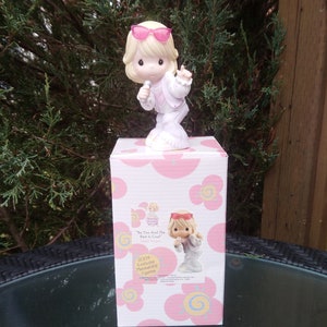 May include: A white porcelain figurine of a girl wearing pink sunglasses and a white jacket, holding a microphone. The figurine is on top of a pink and white box with the text "You're So Cool!" and "Precious Moments" on it.