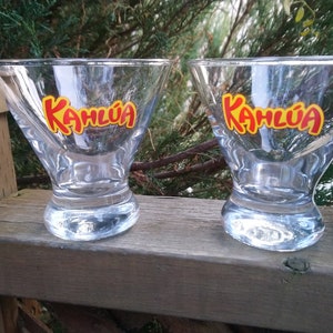 May include: Two clear glass martini glasses with the word "Kahlúa" printed in red and yellow on the front of each glass.