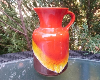Könnte beinhalten: Eine rote, gelbe und braune Keramikvase mit Henkel. Die Vase hat eine glasierte Oberfläche und ein einzigartiges Farbmuster.