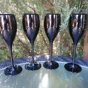 May include: Four black champagne flutes on a woven table top. The flutes are made of glass and have a clear, reflective surface.