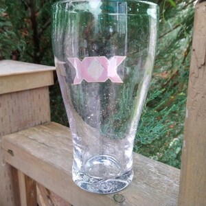 May include: A clear glass beer mug with a pink sticker on the front that says "XXX".
