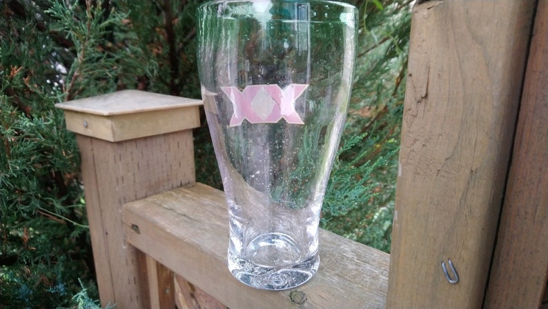 May include: A clear glass beer mug with a pink sticker on the front that says "XXX".