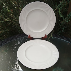 May include: Two white ceramic dinner plates with a fluted edge. The plates are stacked on top of each other.
