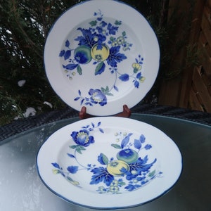 May include: Two white ceramic soup bowls with blue and green floral designs. The bowls have a blue rim and feature a floral pattern with yellow and green accents.