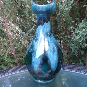 Op de afbeelding: Een tealblauwe keramische vaas met een brede opening en een peervormig lichaam. De vaas heeft een glanzende afwerking en een draaiend patroon.