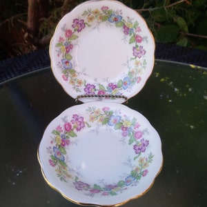 May include: Two white porcelain bowls with a floral pattern in shades of pink, blue, and yellow. The bowls have a scalloped edge and a gold trim.