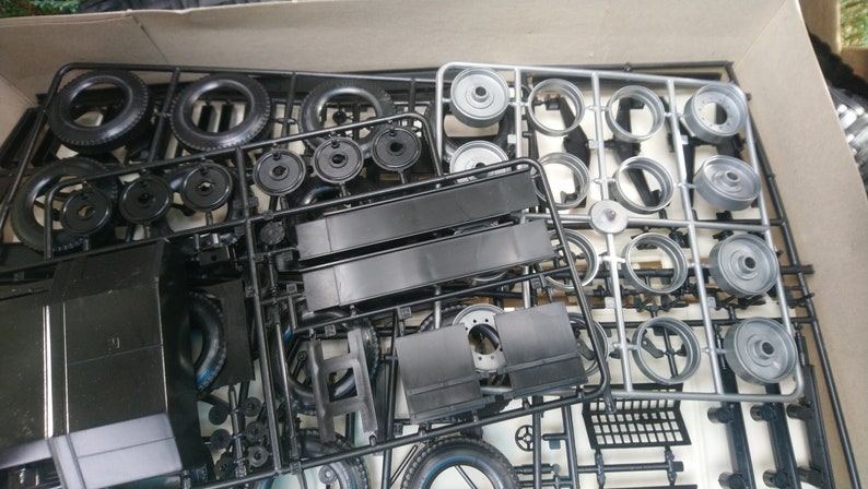 May include: A model kit with various black and silver plastic parts, including tires, wheels, and body components. The parts are still attached to their plastic frames, ready for assembly. The kit is in a cardboard box.