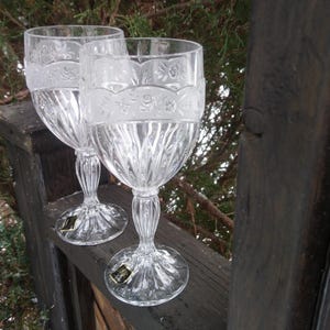 May include: Two clear glass wine glasses with intricate etched designs. The glasses have a tall, slender stem and a wide bowl.