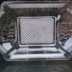 May include: A clear glass serving tray with a raised diamond pattern and a decorative design of deer in the center. The tray has a scalloped edge.