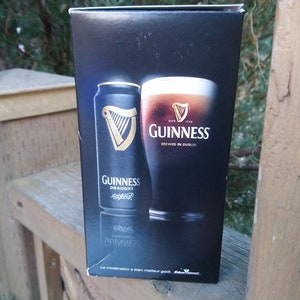 May include: A black box with a can and a glass of Guinness beer. The can says "Guinness Draught" and the glass says "Guinness Brewed in Dublin".