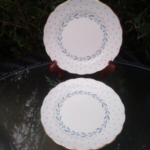 May include: Two white ceramic plates with a blue and grey floral design and gold trim. The plates have a white background with small blue dots.