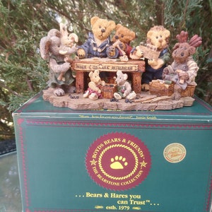 May include: A figurine of a group of bears and a moose gathered around a table, with the text "Home & Ark Aulders" on the table. The figurine is on a box with the text "Boyd's Bears & Friends The Bearstone Collection Bears & Hares you can Trust™ estb. 1979".