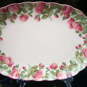 Puede incluir: Plato ovalado blanco para servir con un diseño floral rosa y verde alrededor del borde. El plato tiene un borde festoneado.