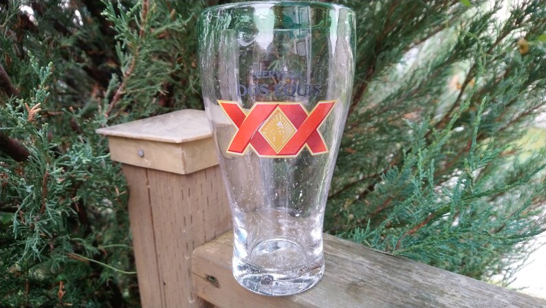 May include: A clear glass beer mug with a red and gold logo that says "Cerveza Dos Equis" and "XX".