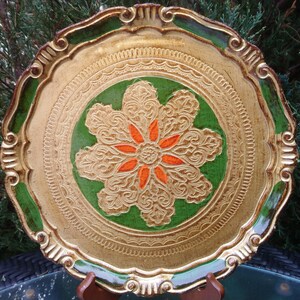 Puede incluir: Una bandeja decorativa dorada y verde con un diseño de flor naranja en relieve y adornado en el centro.