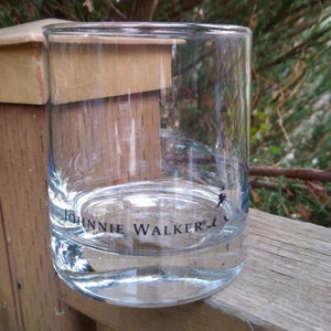 K&ouml;nnte beinhalten: Ein klares Glas mit der Aufschrift "Johnnie Walker" auf dem Boden. Das Glas steht auf einer Holzoberfl&auml;che.