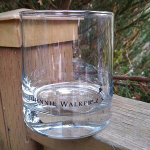 K&ouml;nnte beinhalten: Ein klares Glas mit der Aufschrift "Johnnie Walker" auf dem Boden. Das Glas steht auf einer Holzoberfl&auml;che.